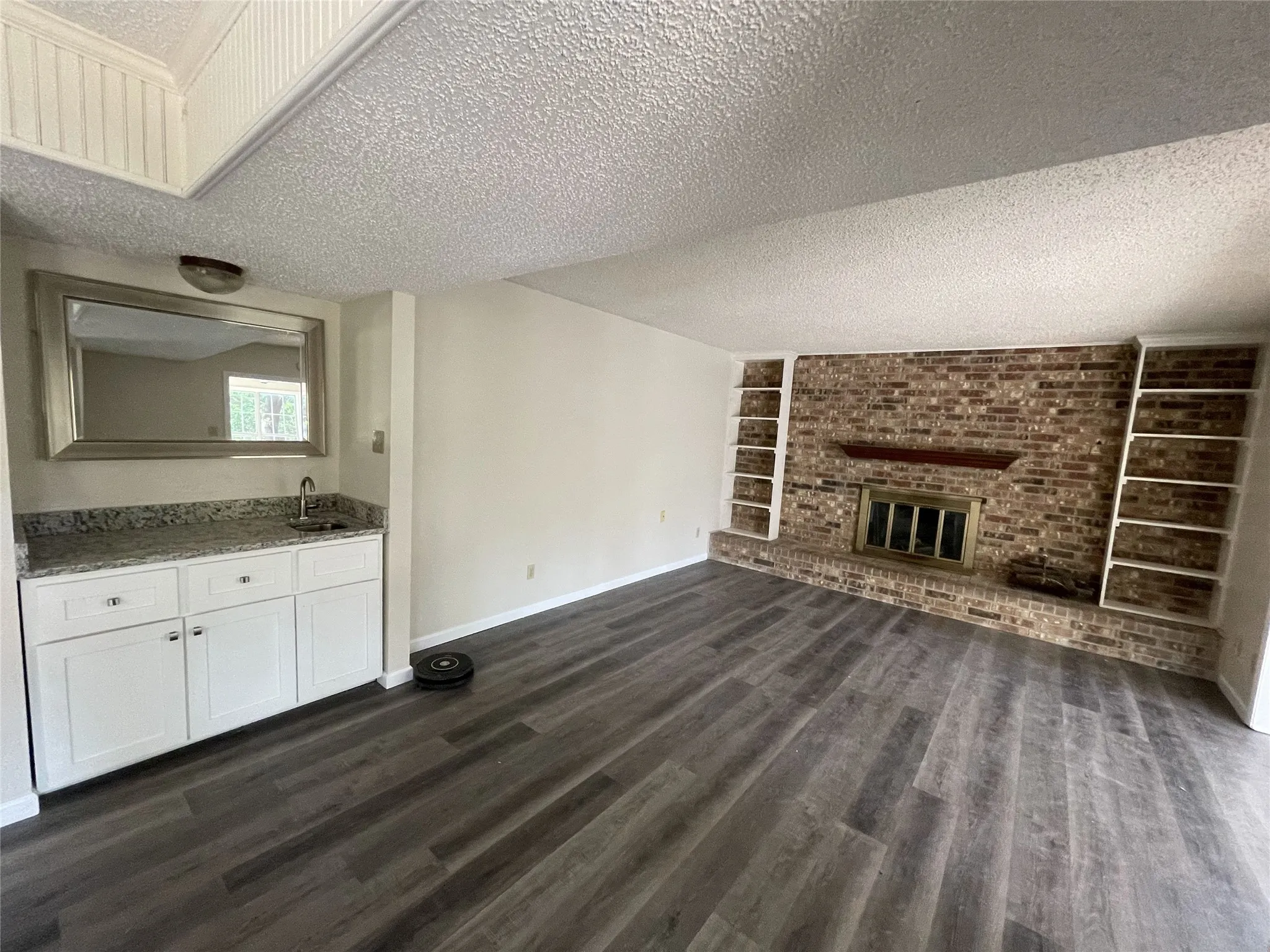 Brick fireplace with hearth, built-in shelving, wood-finish flooring, wet bar with granite countertop, and white cabinetry