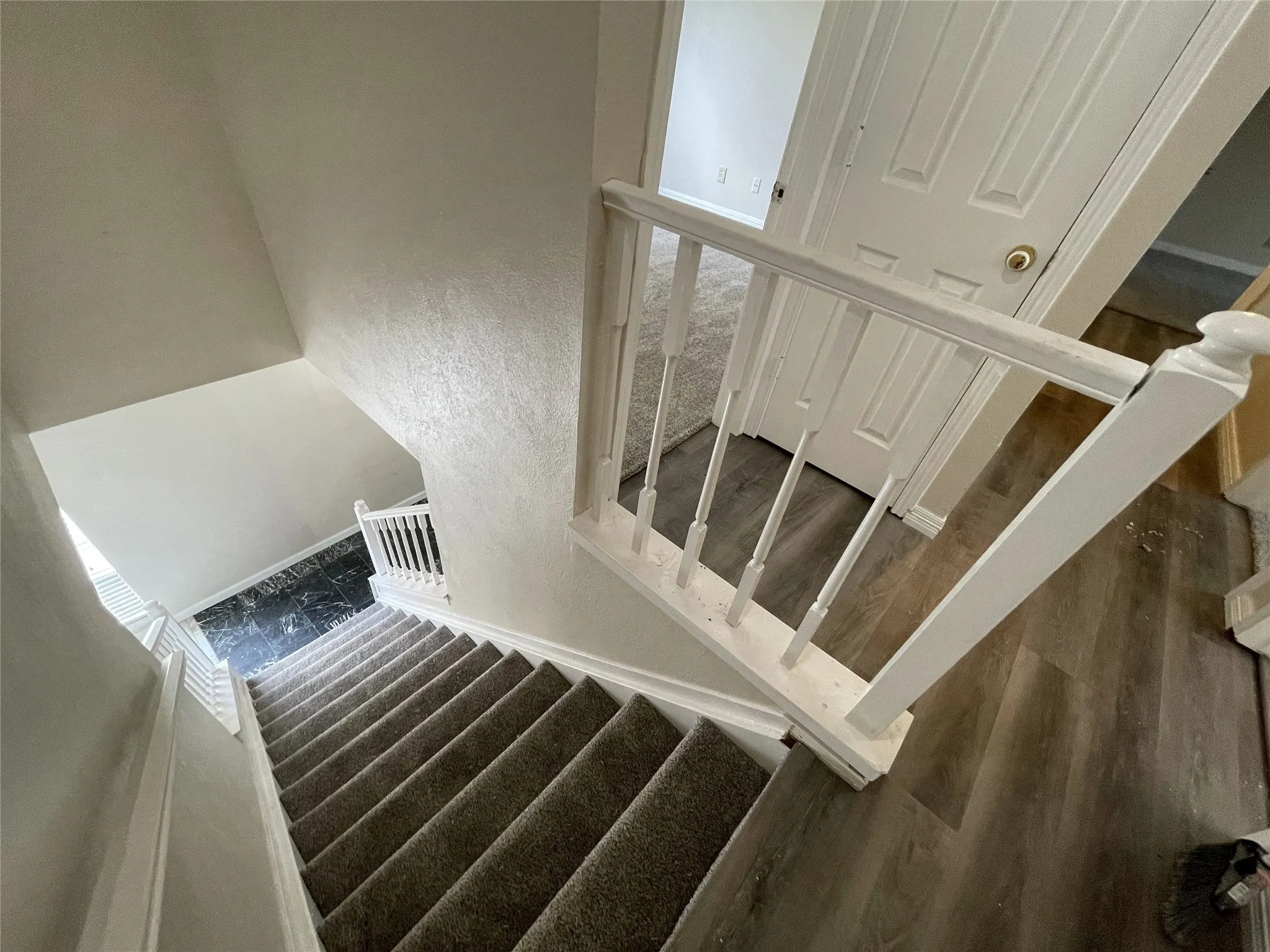 Carpeted staircase with white balusters and handrails, leading to wood-finish flooring
