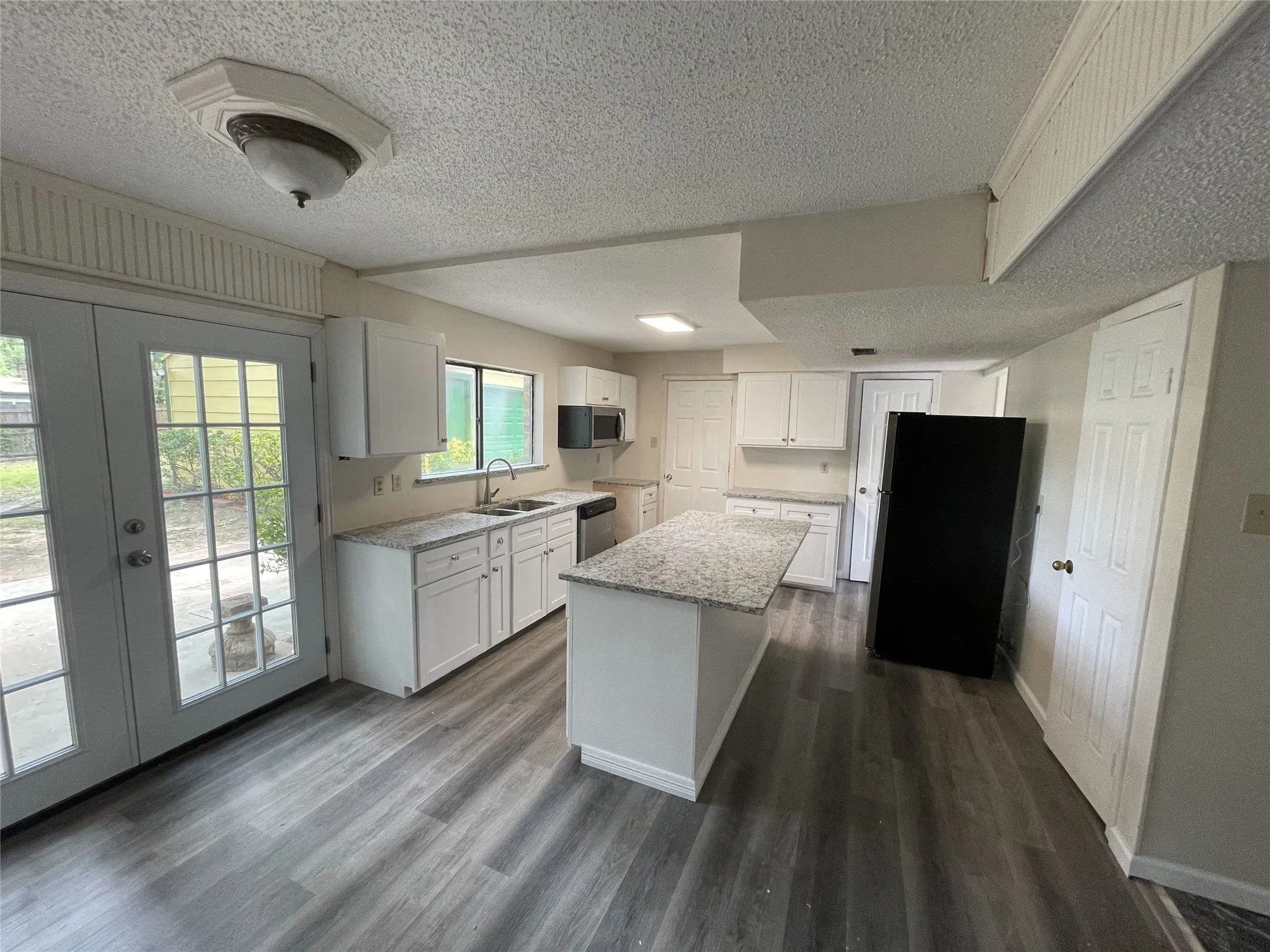 Kitchen featuring white cabinetry, gray wood-finish flooring, a central island with a light-colored countertop, and a stainless steel sink with a gooseneck faucet