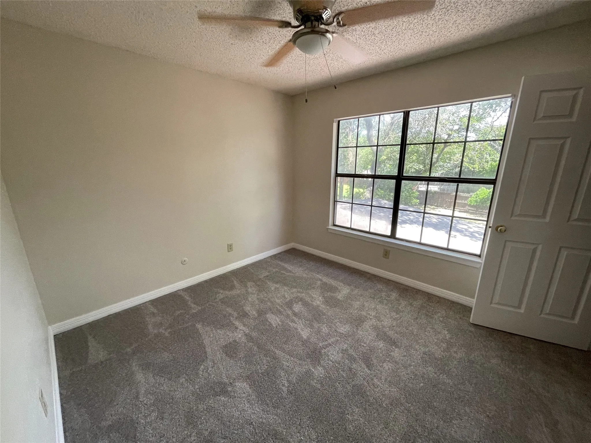 Ceiling fan with integrated light fixture, neutral wall paint, carpet flooring, window with multiple panes, paneled interior door