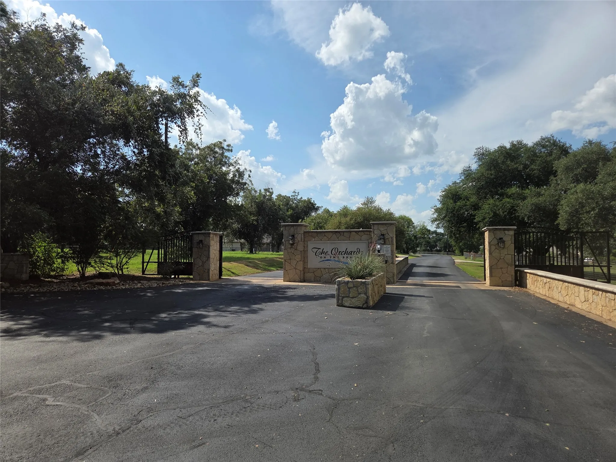 Gated entry with stone pillars, stone-clad retaining walls, and mature landscaping