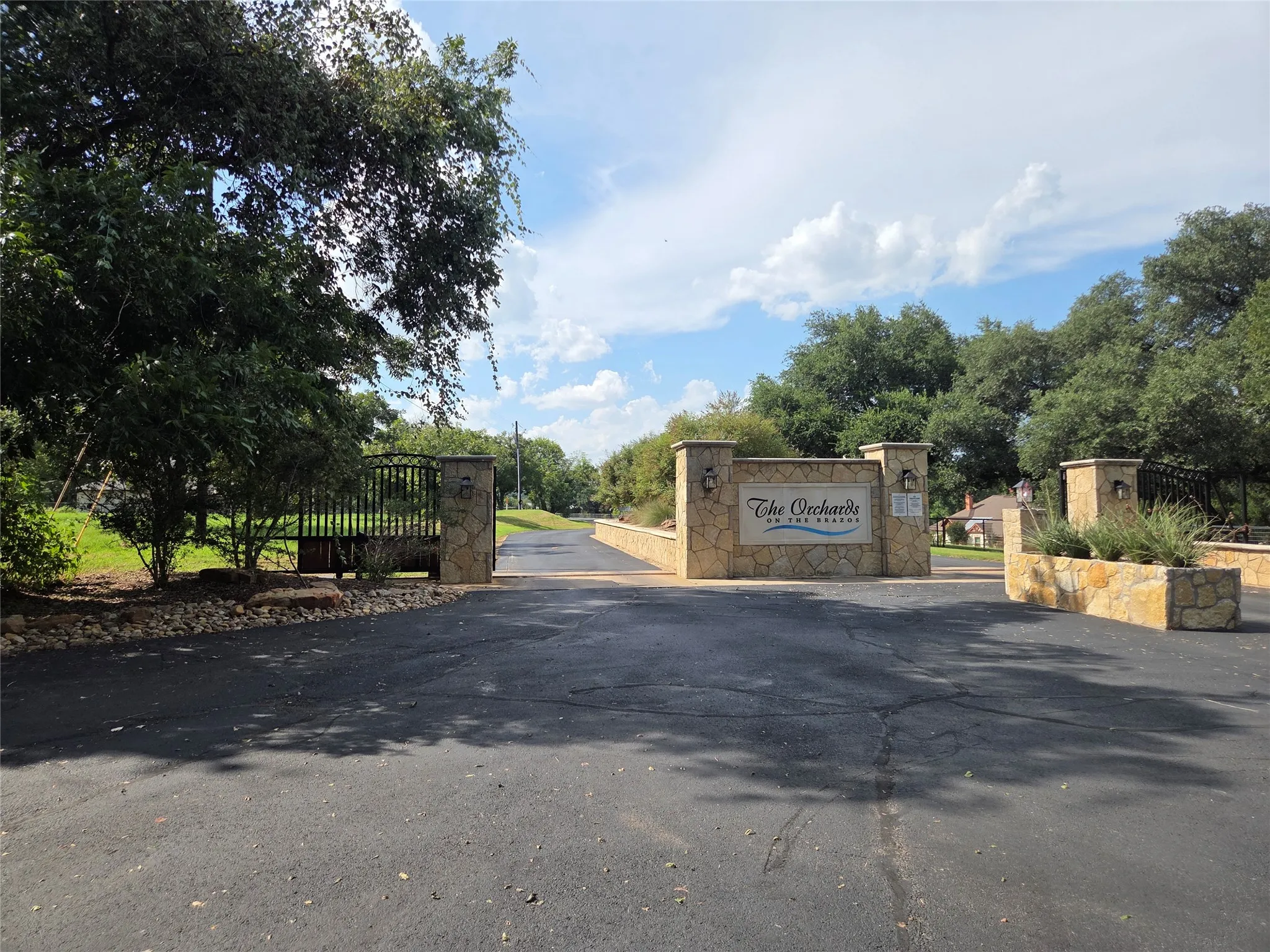 Paved entry with stone signage, stone planter boxes, and a wrought iron gate