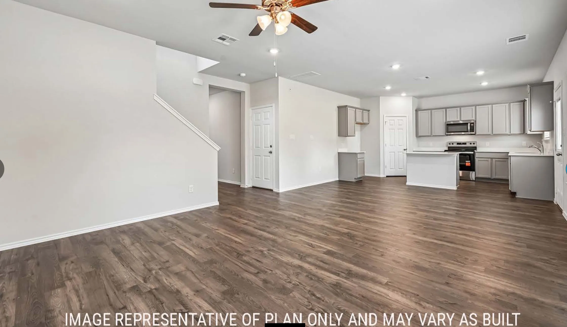Wood-finish flooring throughout, ceiling fan with integrated lighting, recessed lighting, white stair railing, and a kitchen featuring gray cabinetry, stainless steel appliances, and an island with counter seating