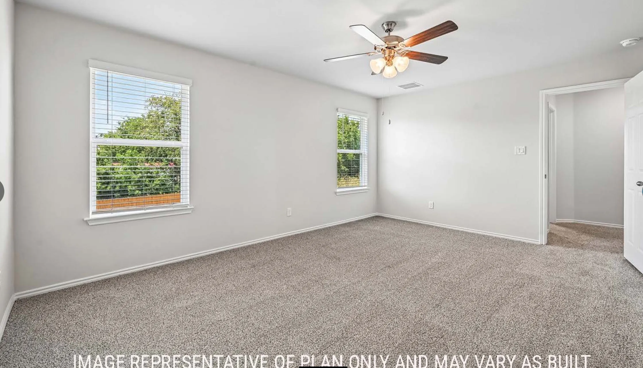 Spacious room featuring carpeting, two windows with blinds, a ceiling fan with integrated lighting, and a white interior door