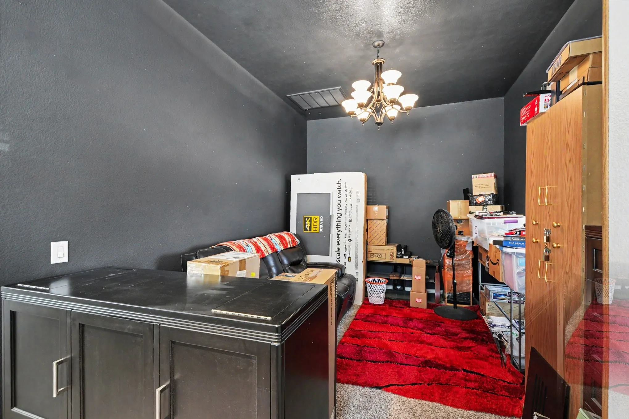 Recessed ceiling with an ornate chandelier, dark wall finish, and built-in cabinetry with metal pulls