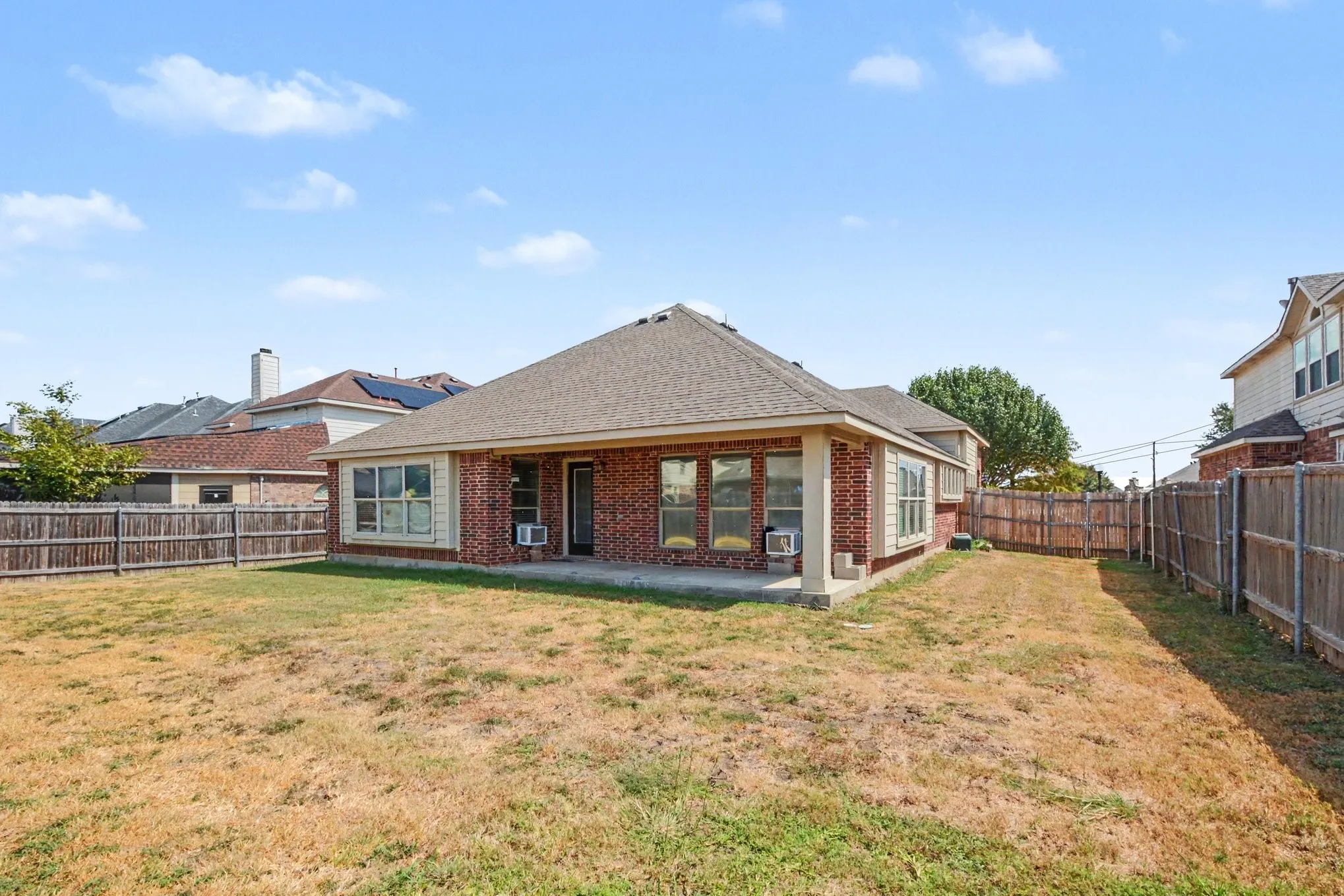 Expansive backyard featuring a red brick exterior, covered patio, and perimeter fencing