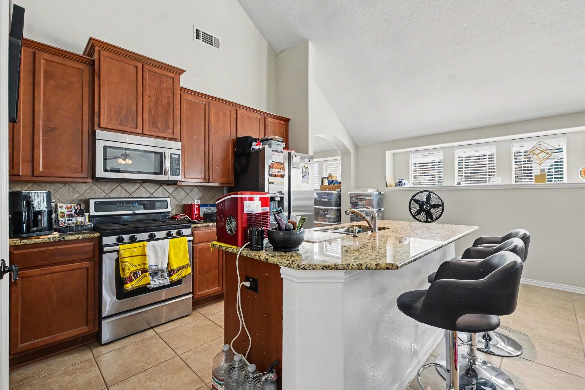 Kitchen featuring a gas range, built-in microwave, wood cabinetry, granite countertops, and tile flooring
