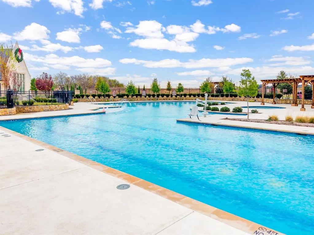 Expansive outdoor swimming pool with surrounding concrete decking, multiple water features, and decorative pergolas
