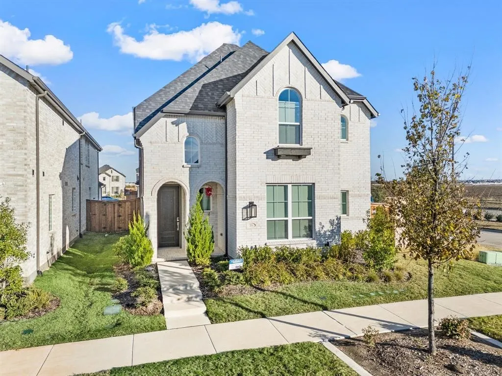 White brick exterior with arched entryway, dark wood-finish front door, arched windows, rectangular windows, and a gray shingled roof