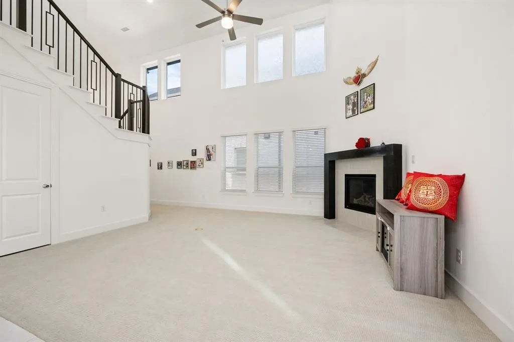 Vaulted ceilings with a ceiling fan, fireplace with a dark mantel, multiple windows, and a staircase with an open-rail design