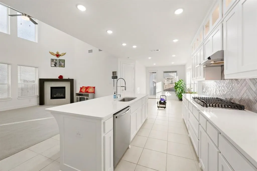 Kitchen featuring white cabinetry, a gas range with stainless steel hood, an island with an integrated sink and dishwasher, and a herringbone pattern tile backsplash