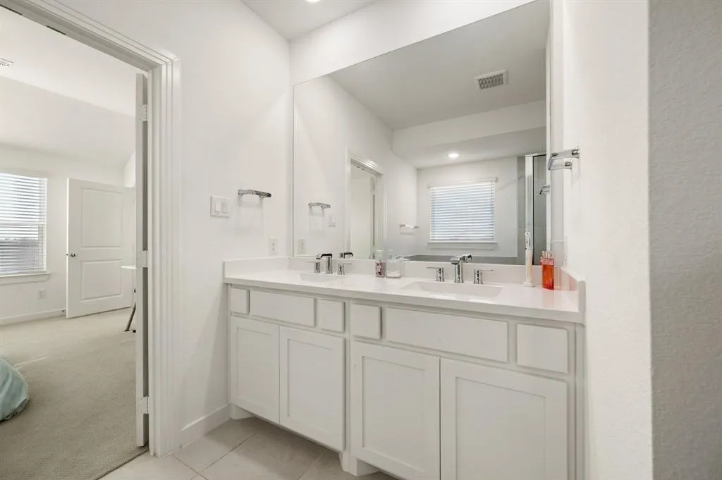 Dual vanity with white cabinetry, polished chrome fixtures, and a large wall-mounted mirror