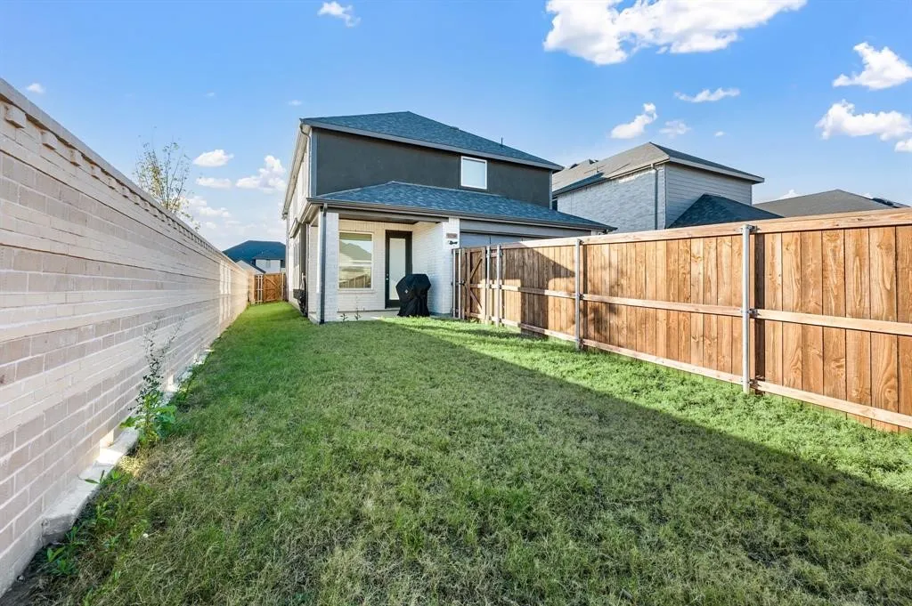 Grassed backyard with a brick privacy wall, wood plank fencing, and a covered patio area