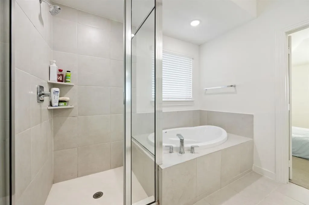 Walk-in shower with clear glass enclosure and integrated shelving, accompanied by a built-in soaking tub featuring a deck-mounted faucet and tiled surround