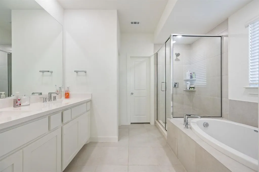 Dual sink vanity with white cabinetry and chrome fixtures, large soaking tub, and a separate glass-enclosed shower
