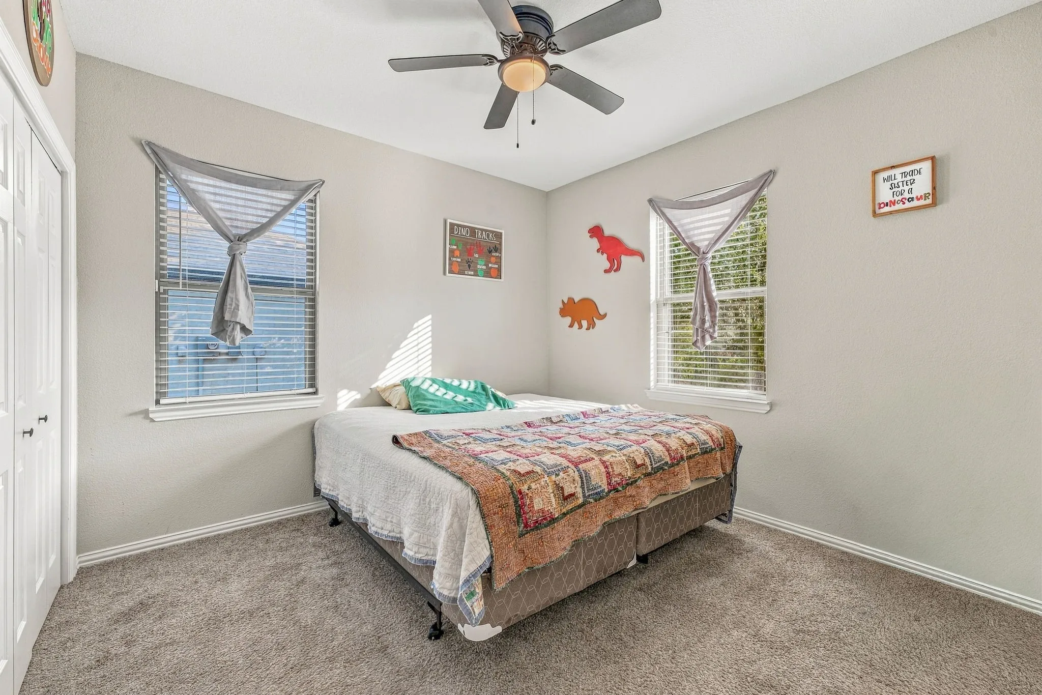 Neutral-toned walls, gray carpet, dual windows with blinds, ceiling fan with light fixture, and white bi-fold closet doors