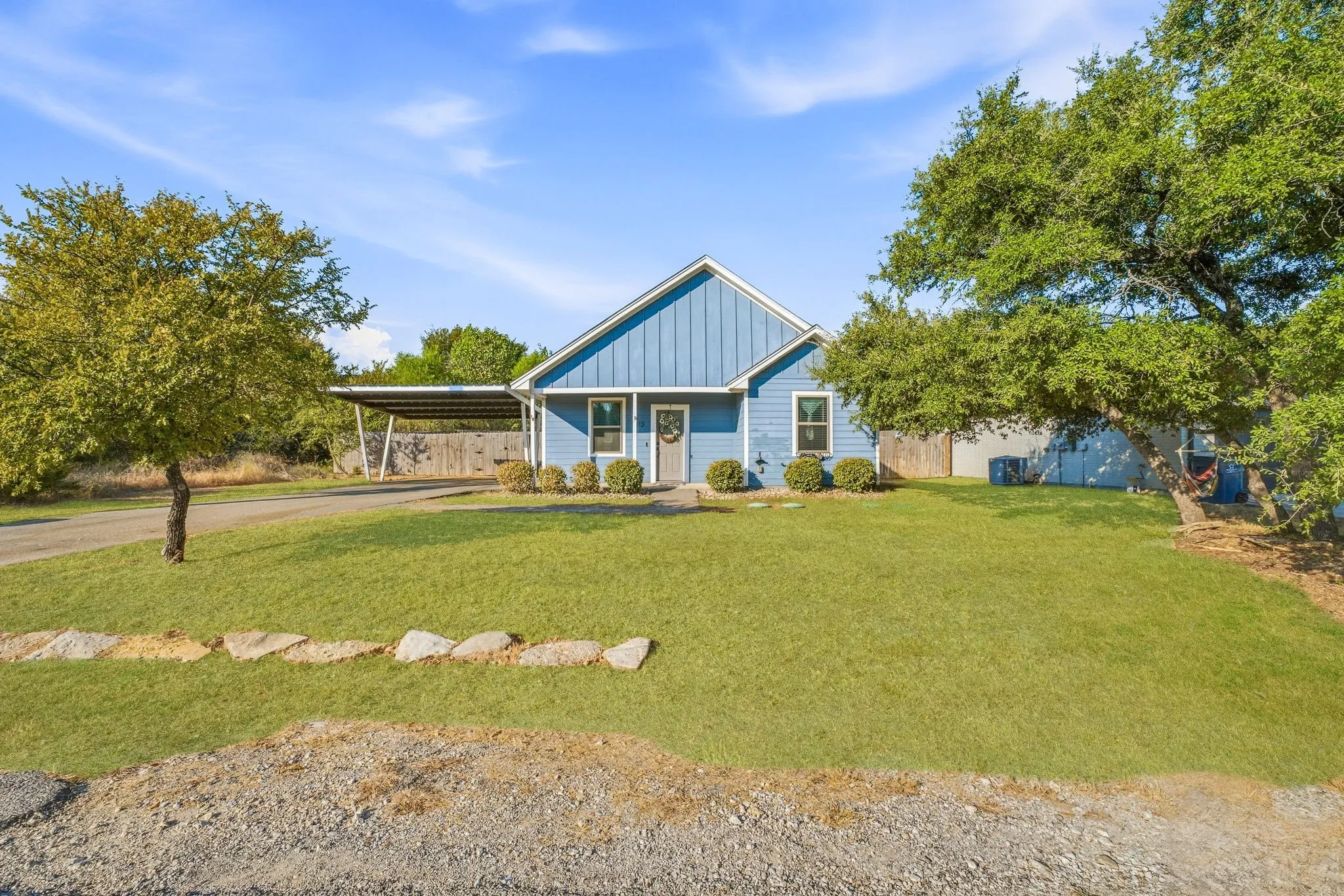 Blue siding exterior with white trim, a covered carport, and a manicured lawn