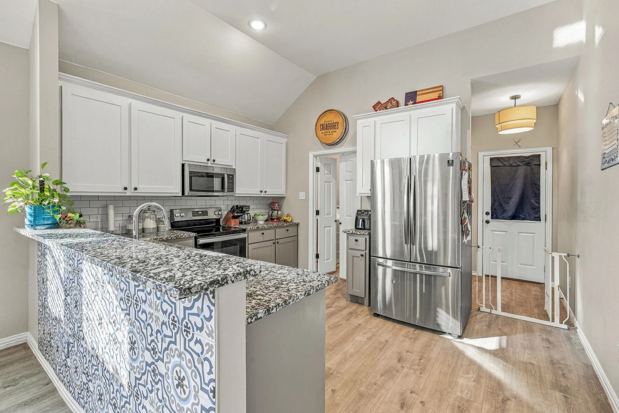 Kitchen featuring white upper cabinetry, a stainless steel microwave, a dual basin sink, wood-finish flooring, and a granite-patterned countertop