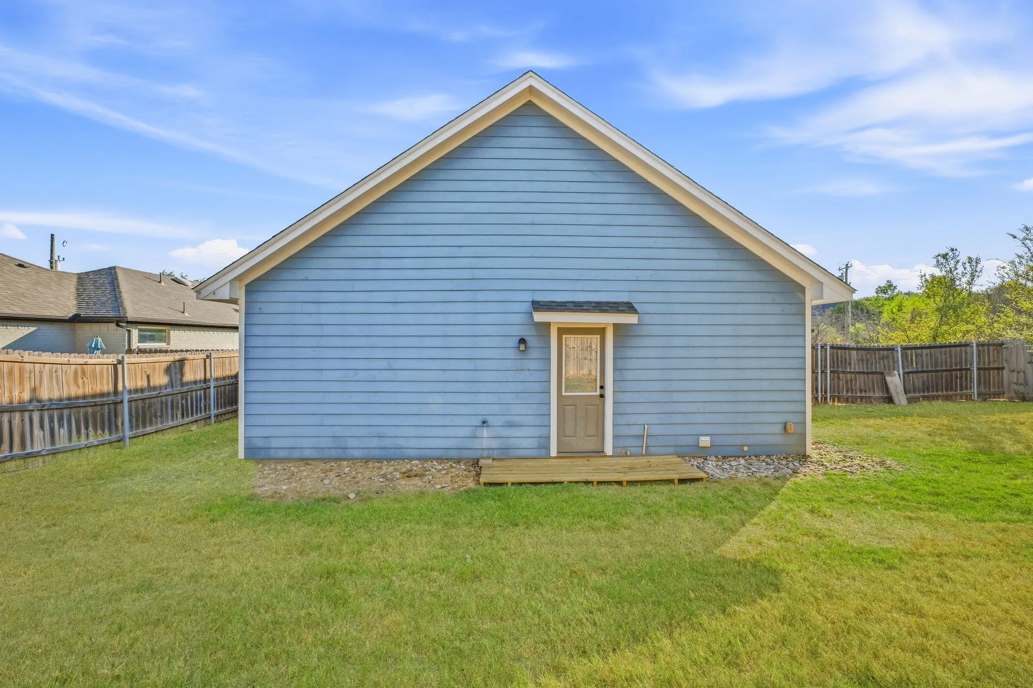Rear exterior featuring blue horizontal siding, a light brown door with a small awning, and a wooden deck