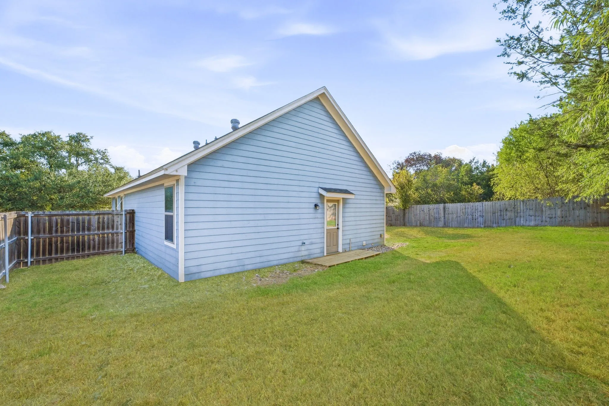 Light blue siding exterior, a gable roofline, a rear entry door with a small awning, a wood deck, and a privacy fence