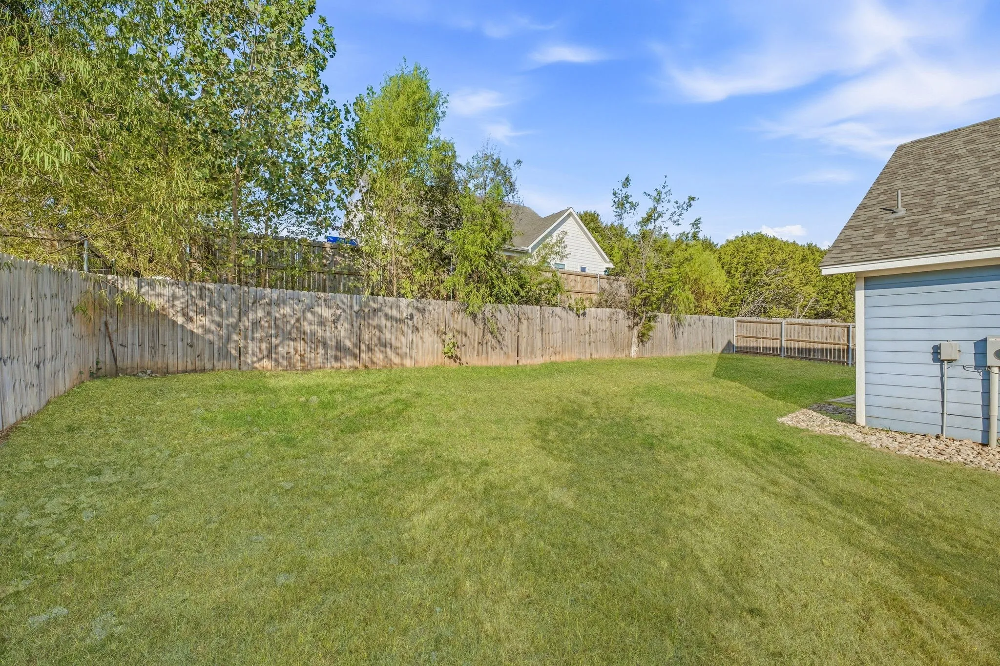 Expansive grassy yard with a wood privacy fence and mature trees
