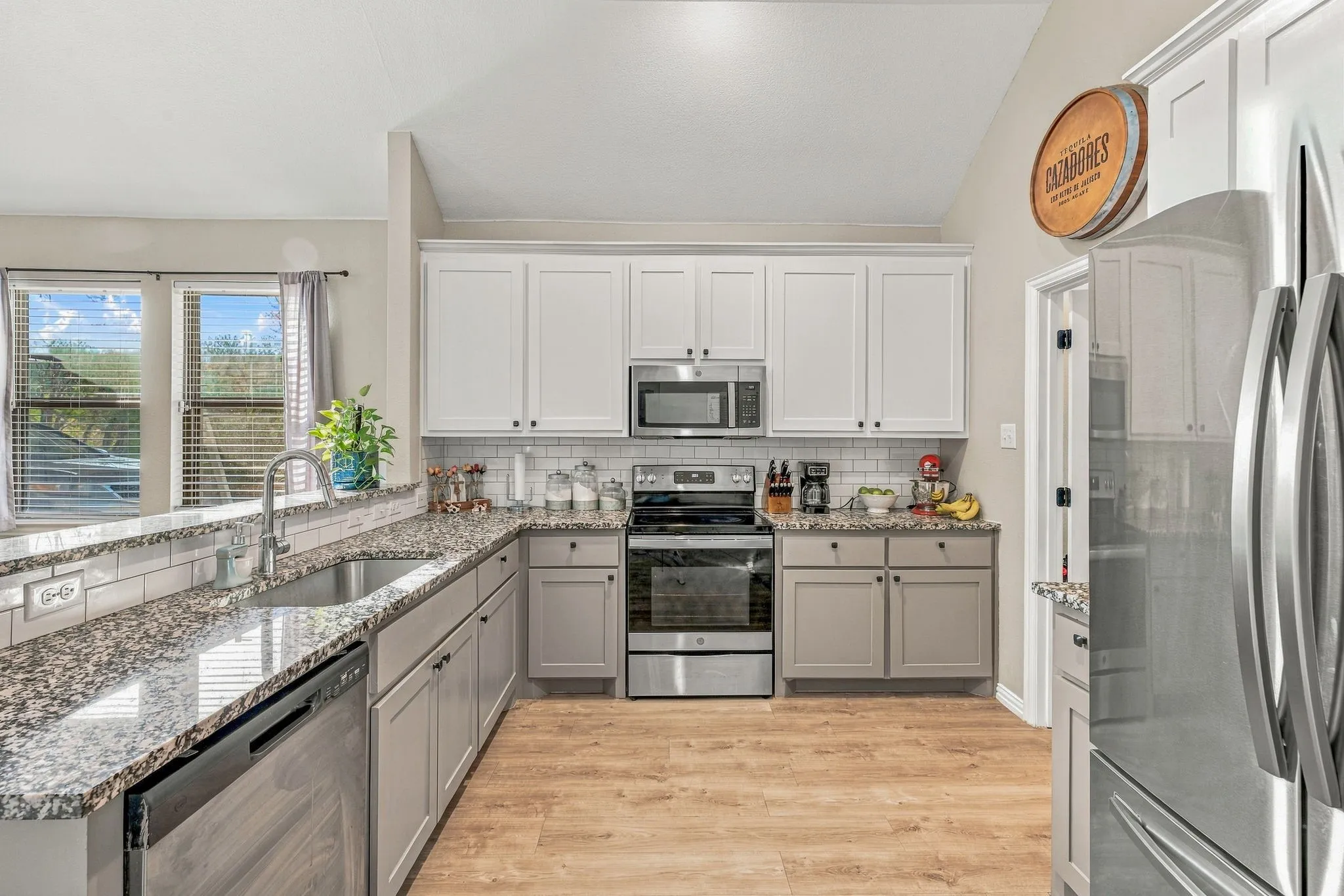 Kitchen featuring wood-finish flooring, two-tone cabinetry, stainless steel appliances, granite countertops, and a subway tile backsplash