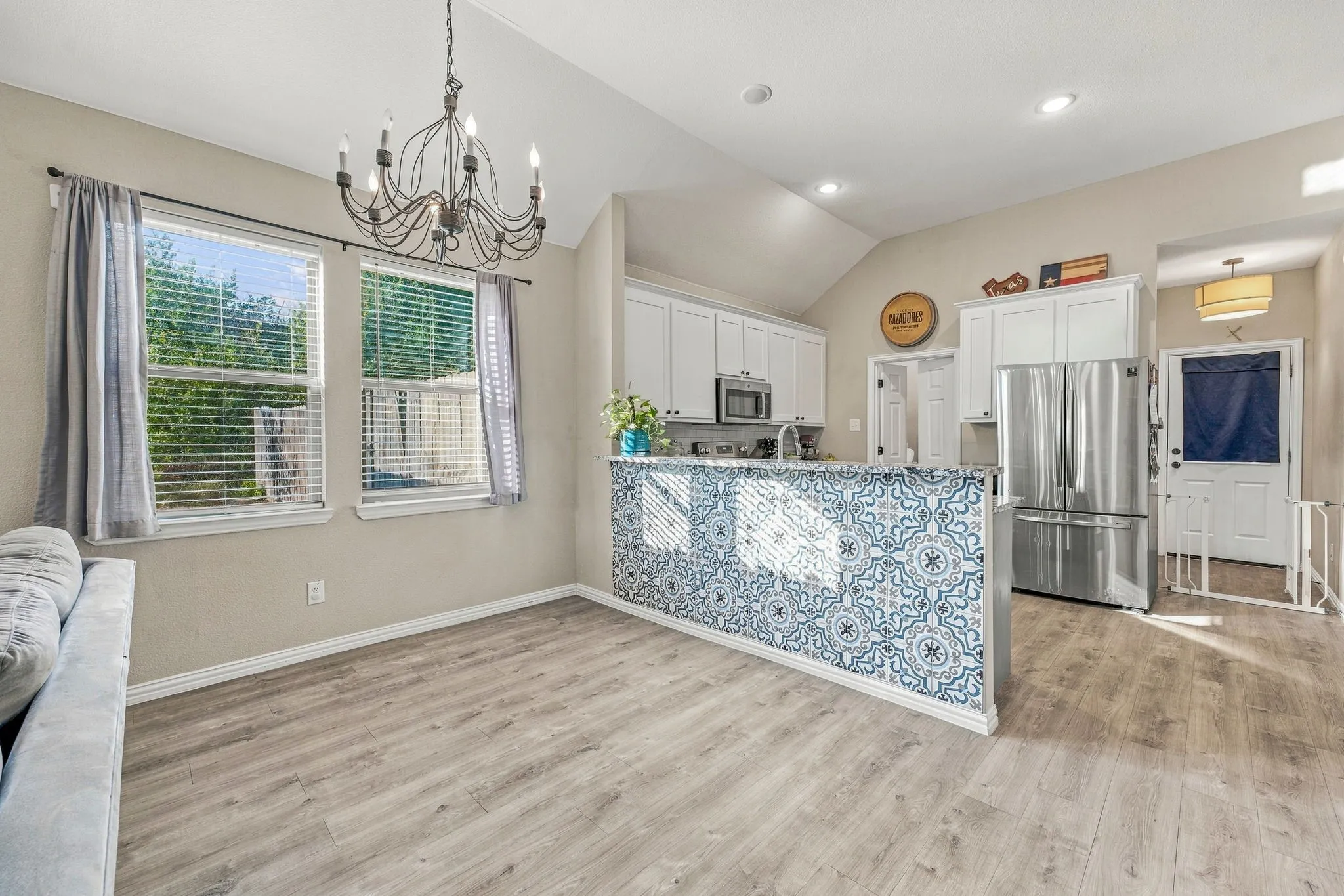 Vaulted ceiling with an iron chandelier, wood-finish flooring, and white cabinetry