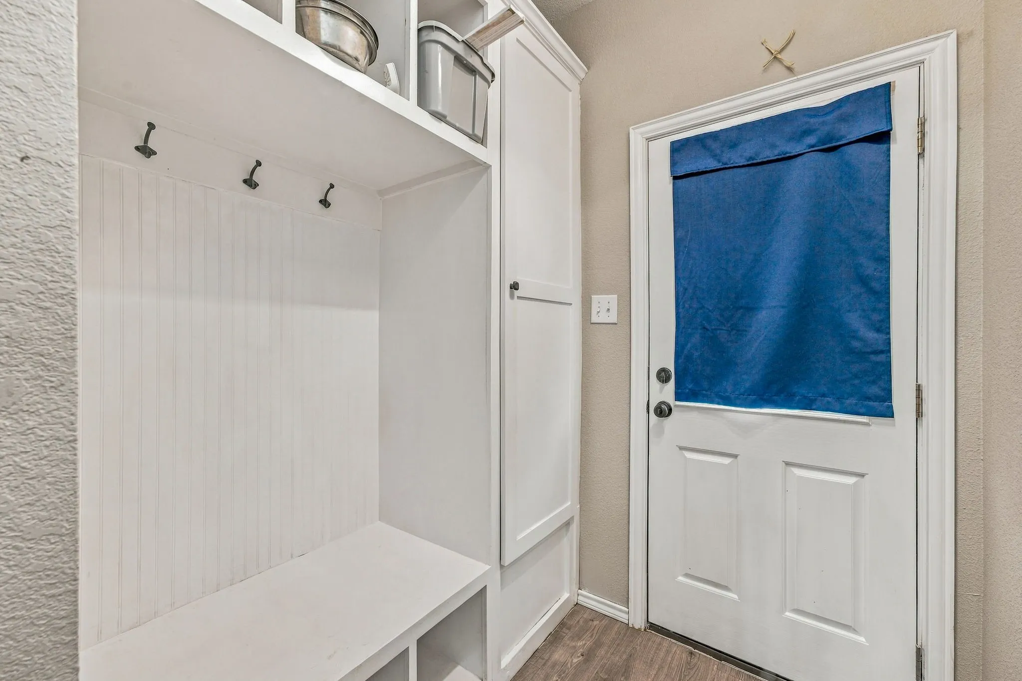 Built-in storage bench with cubbies, white beadboard paneling, and coat hooks