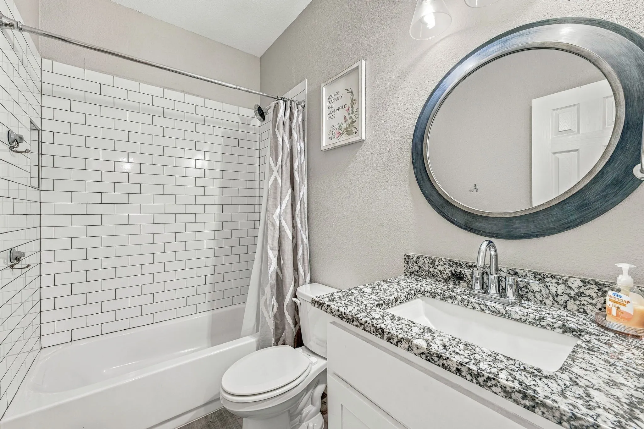 Bathroom featuring a subway tile shower surround, a white bathtub, a single vanity with a granite countertop, a white rectangular sink, and a framed oval mirror