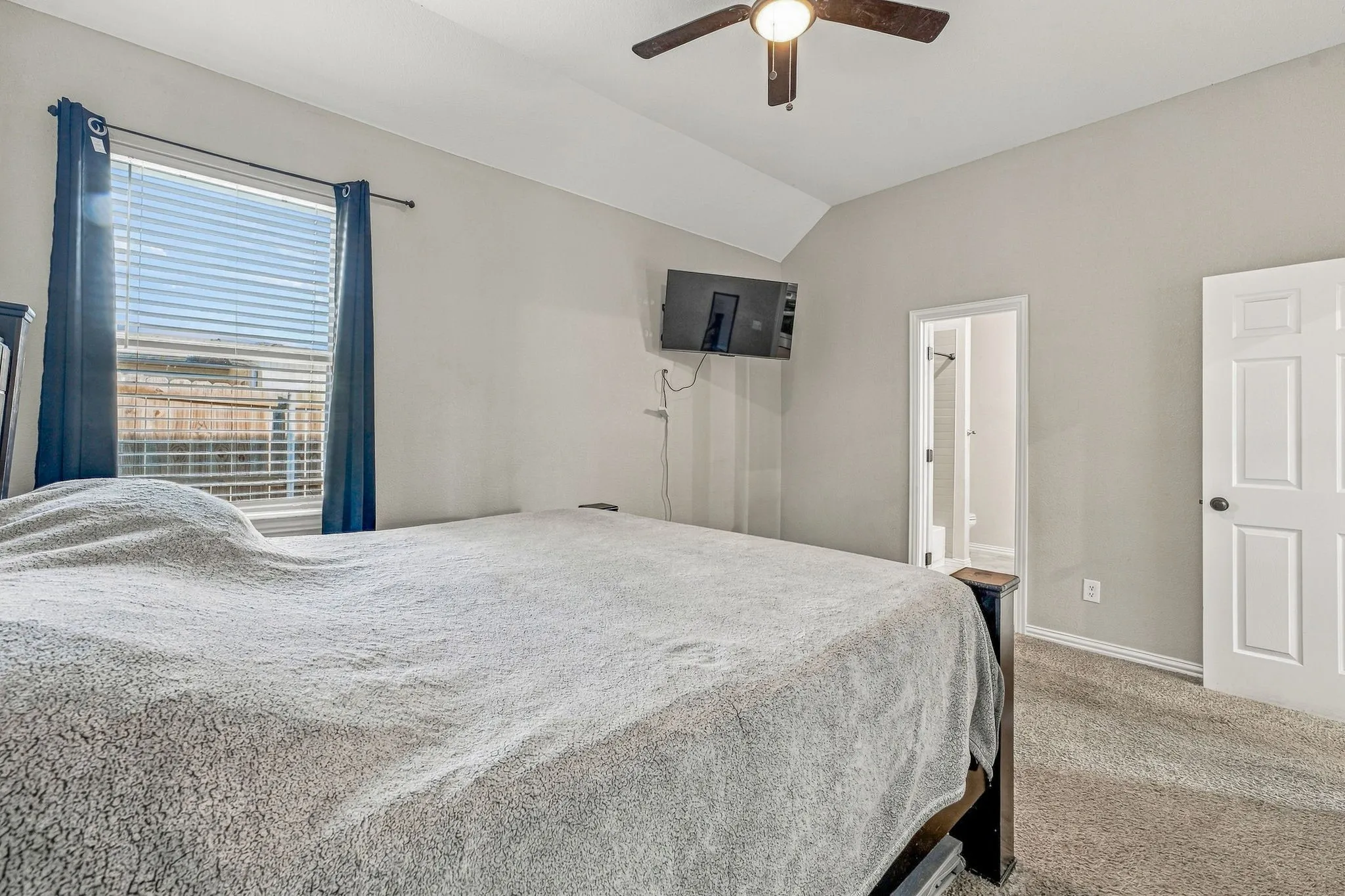 Vaulted ceiling with a ceiling fan, window with blinds, carpet flooring, and a paneled interior door