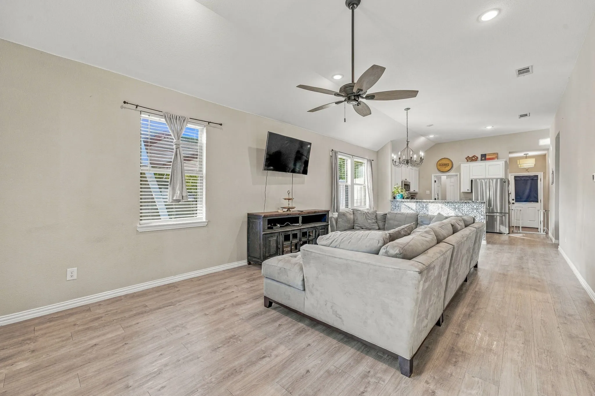 Vaulted ceiling, ceiling fan, recessed lighting, wood-finish flooring, and a kitchen island with a stone-finish countertop
