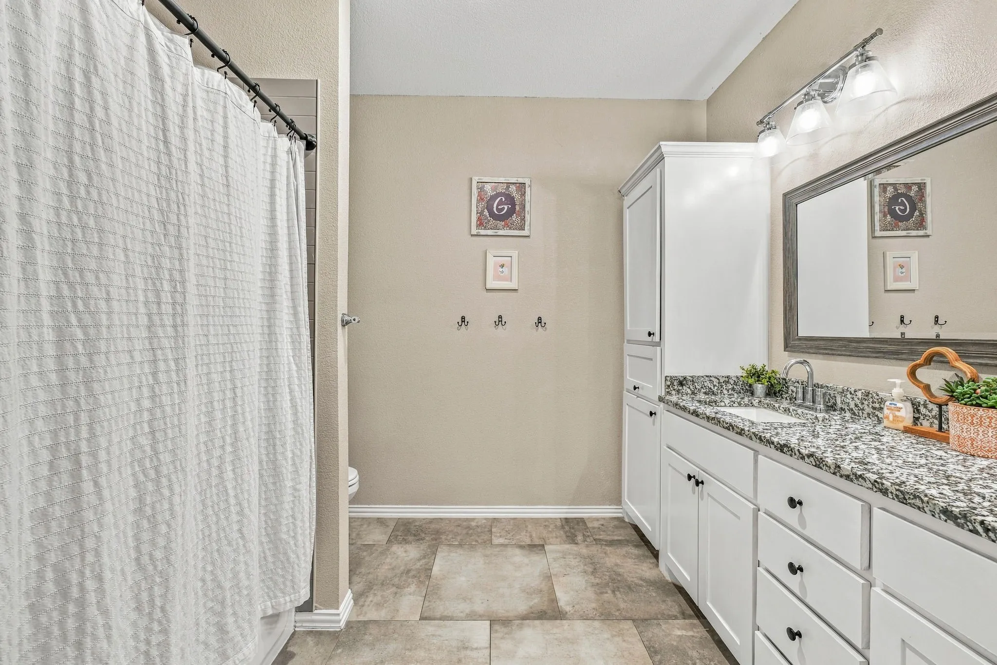 White cabinetry with matte black hardware, granular countertop, rectangular undermount sink, and tiled flooring