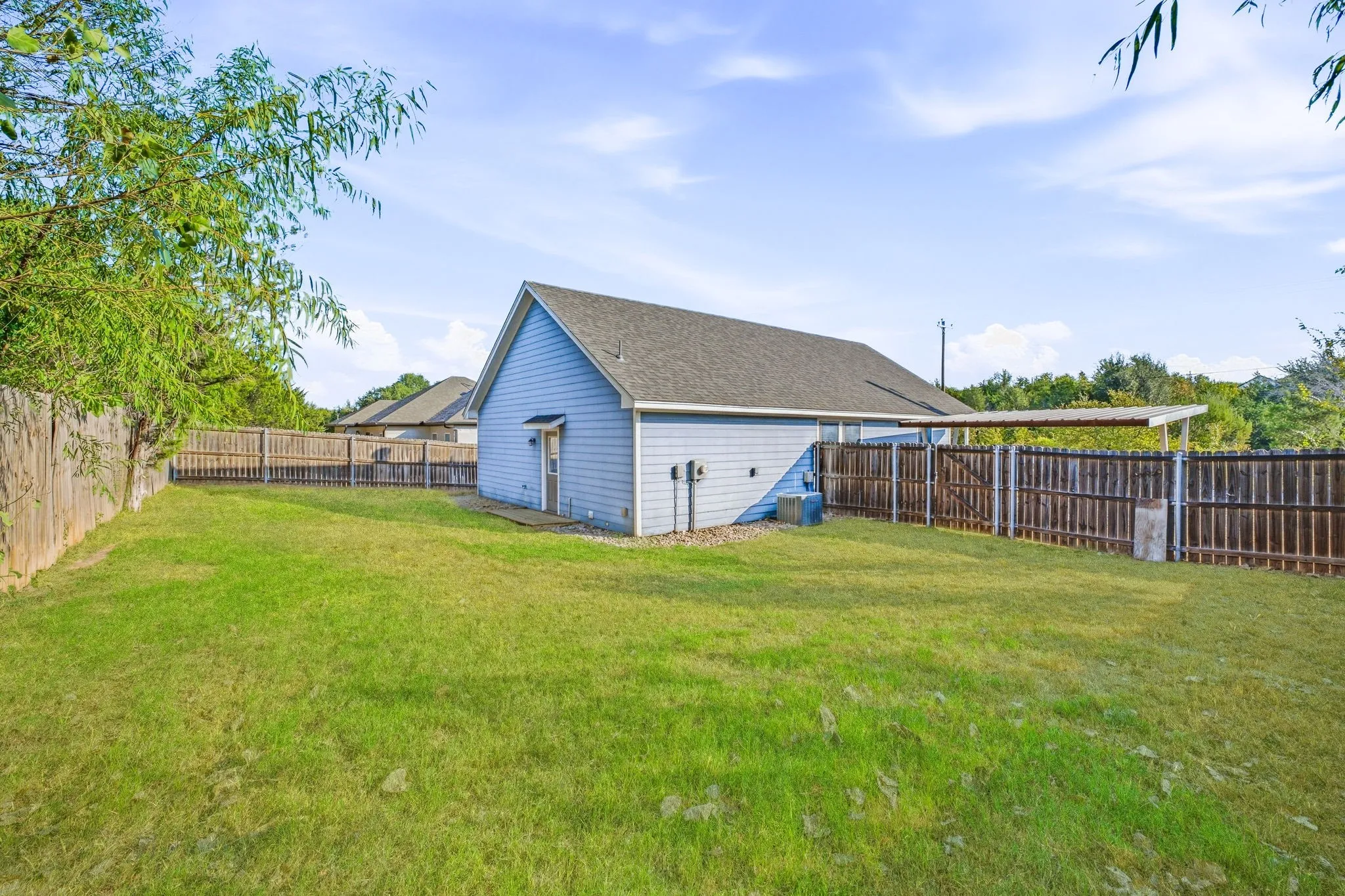 Expansive backyard with a manicured lawn, full perimeter fencing, and a covered patio structure