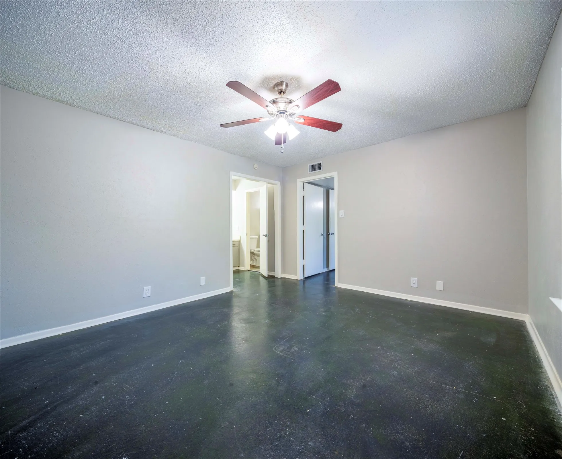 Smooth dark flooring, light gray walls, ceiling fan with integrated lighting, and white trim