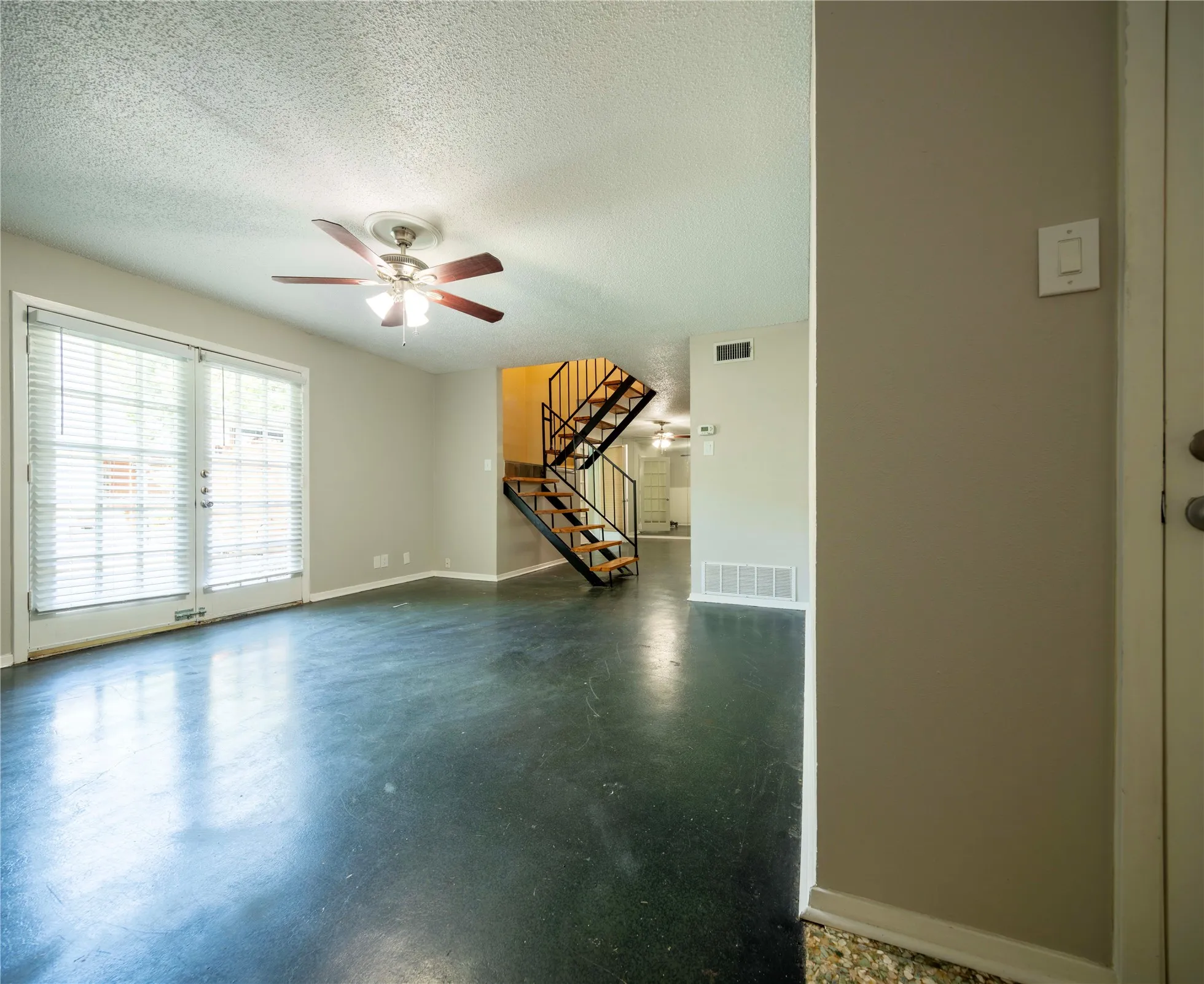 French doors with blinds, ceiling fan with light fixture, open-tread staircase with metal railing, dark-toned flooring, light-colored walls