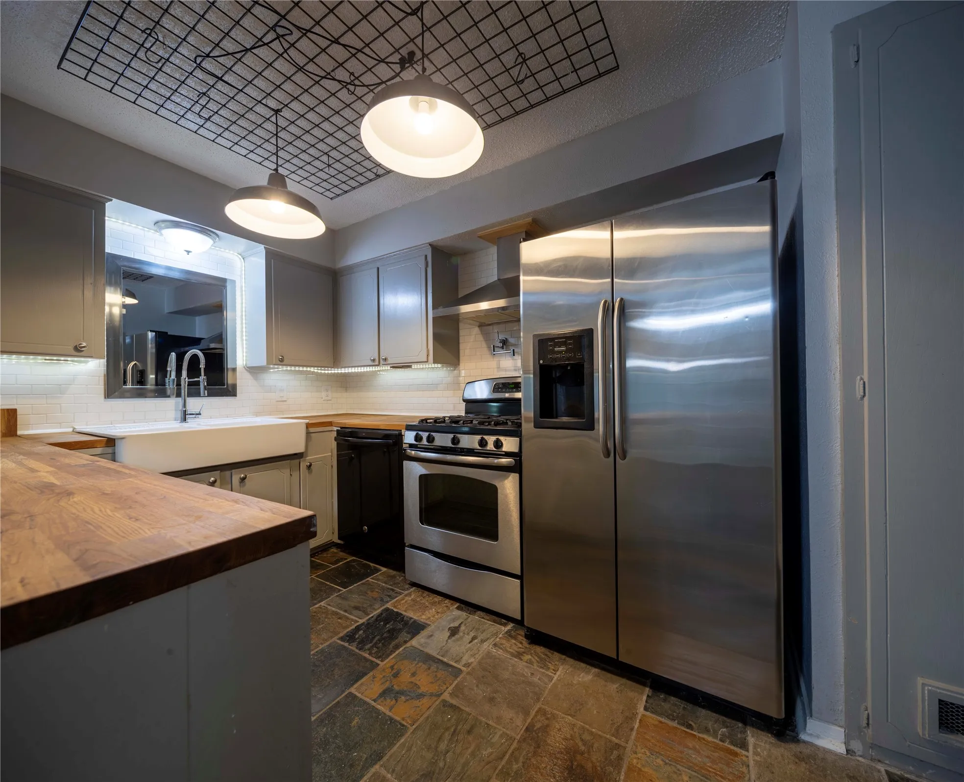Kitchen featuring slate tile flooring, wood-finish countertops, undermount farmhouse sink, stainless steel appliances, and integrated ceiling lighting