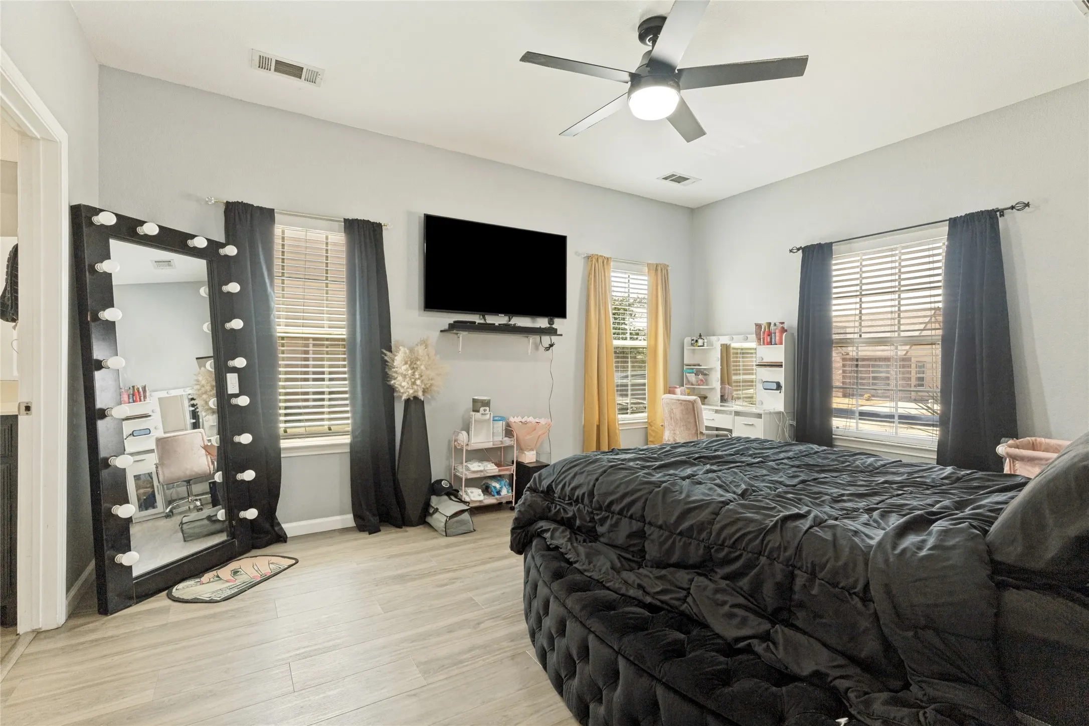 Light-toned wood-finish flooring, a ceiling fan with integrated lighting, and multiple windows with blinds