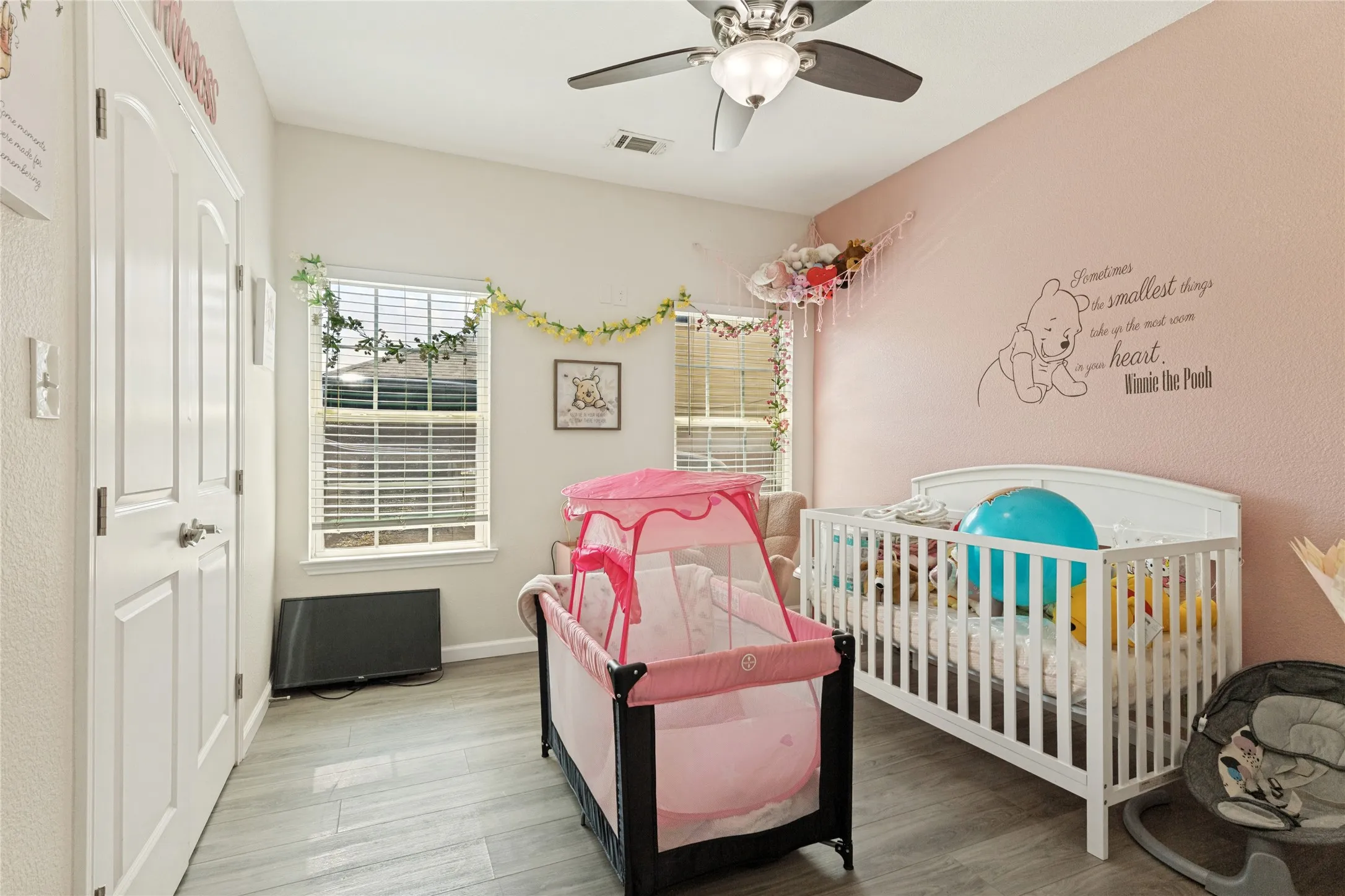Ceiling fan with integrated lighting, wood-finish flooring, white paneled doors, and dual windows with horizontal blinds