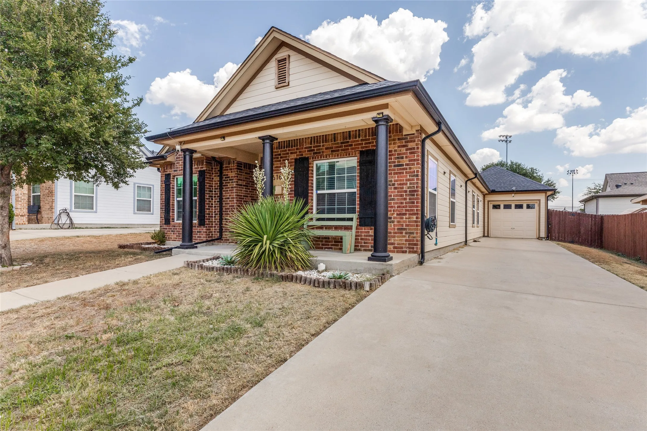 Brick exterior with contrasting trim, covered front porch with decorative pillars, attached garage with a concrete driveway, and a fenced side yard