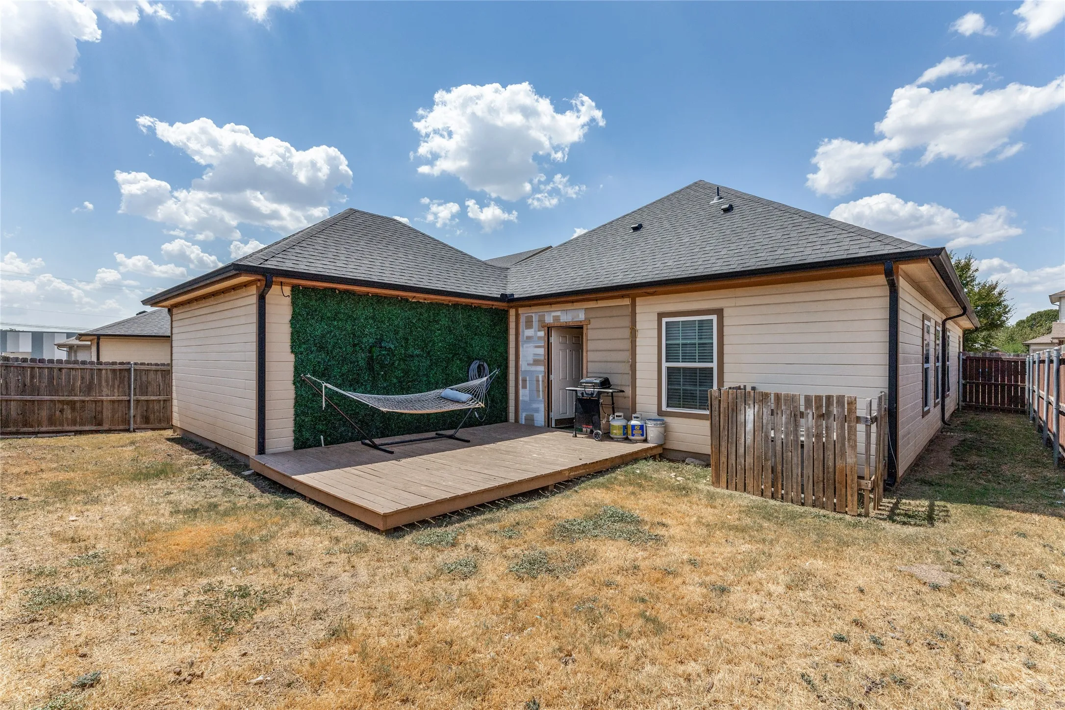 Rear exterior featuring a wood deck, horizontal siding, partial privacy fencing, and a gabled roof