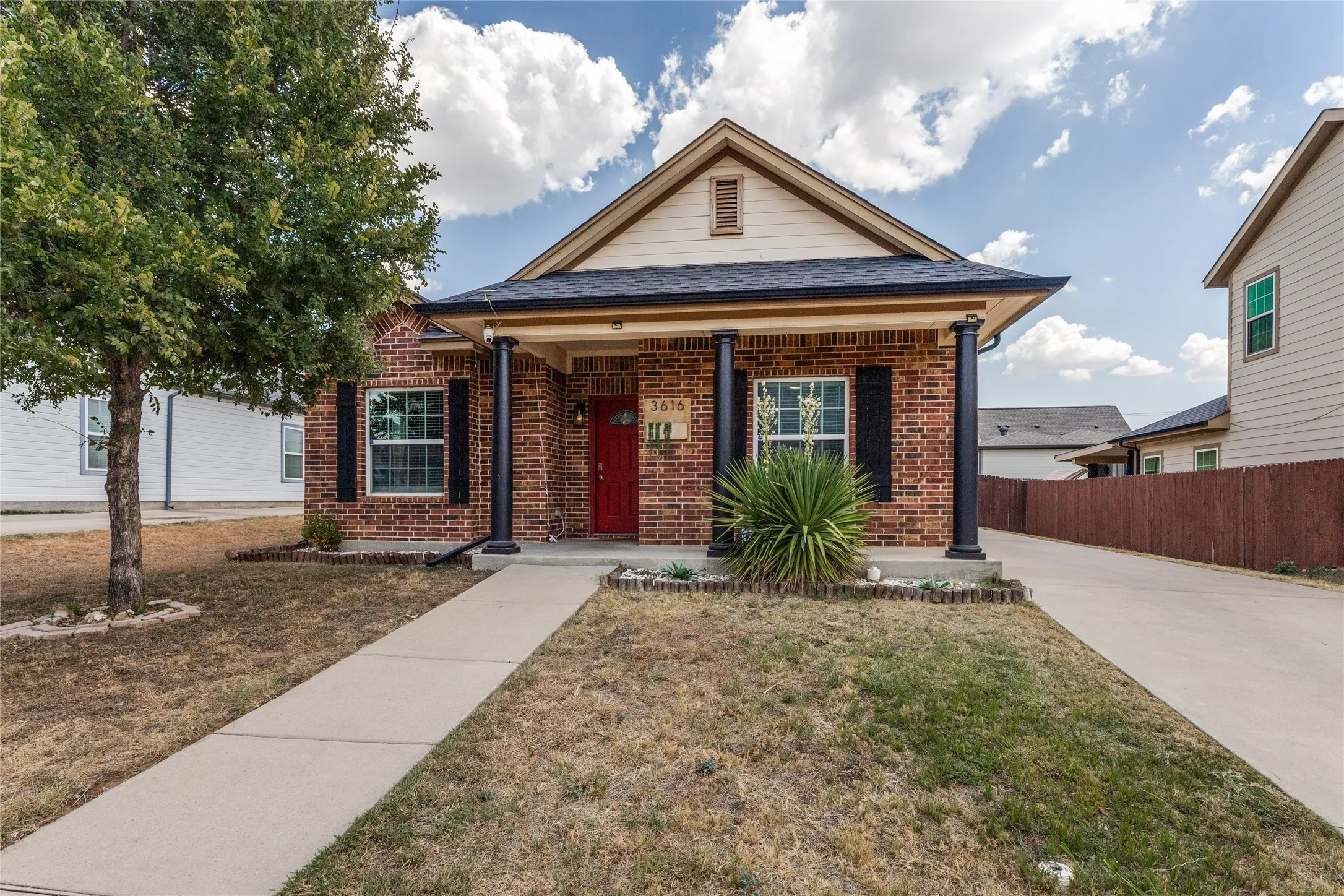Brick exterior with an inviting red entry door, covered front porch, and decorative columns