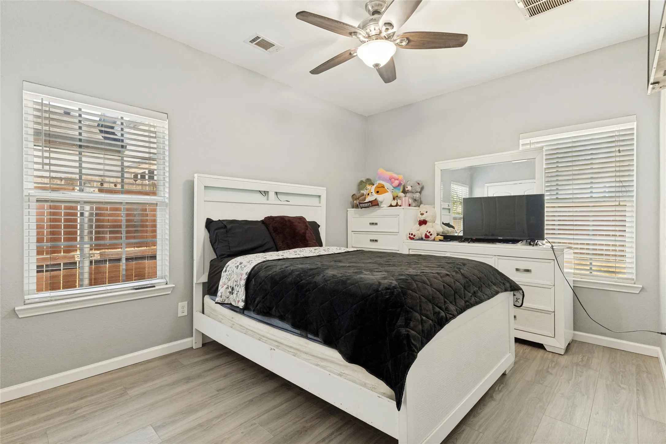 Wood-finish flooring, two windows with blinds, ceiling fan with integrated lighting, and light-toned walls