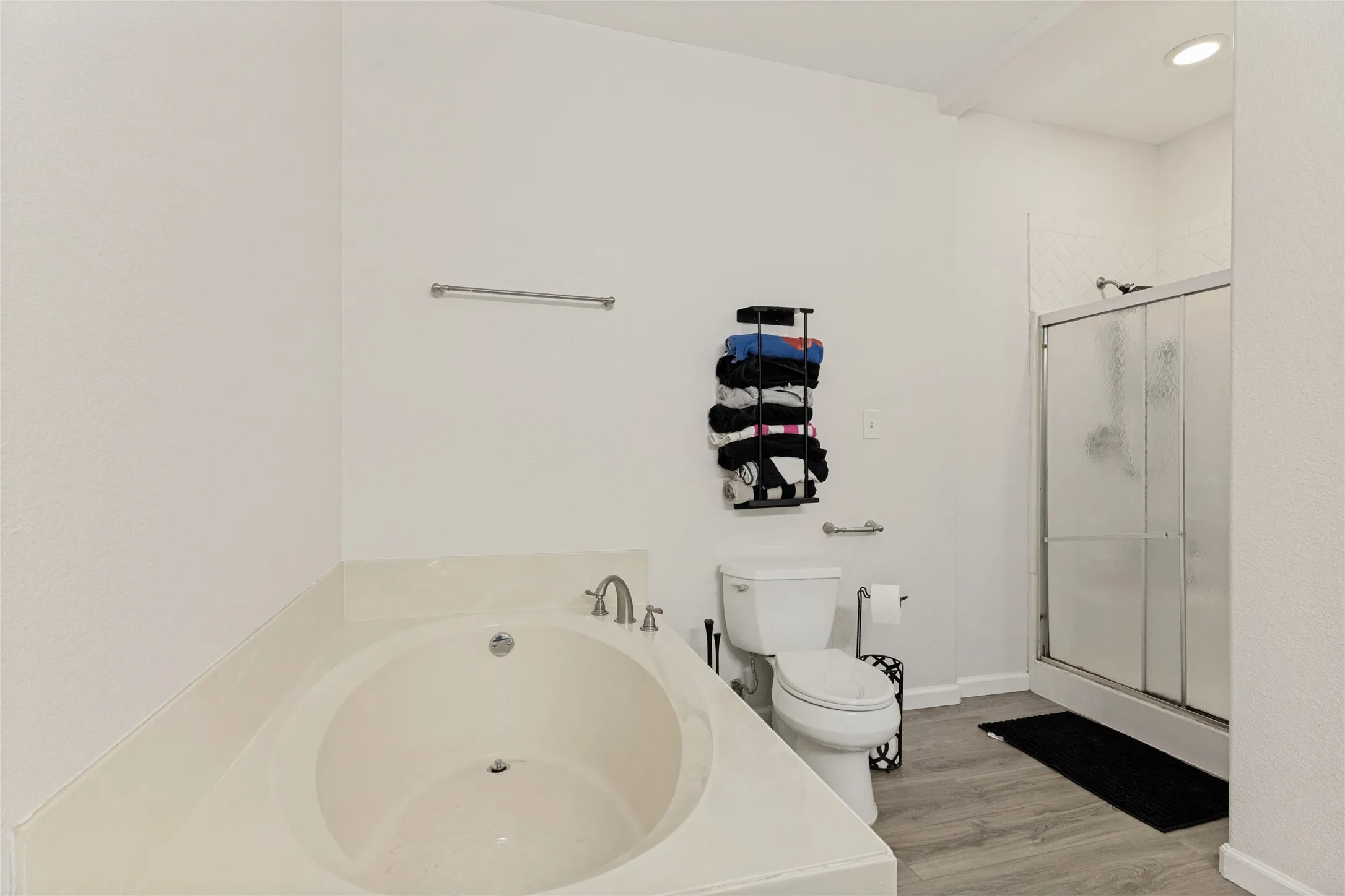 Integrated soaking tub with deck-mounted brushed nickel faucet, glass-enclosed shower, wood-finish flooring, and sloped ceiling
