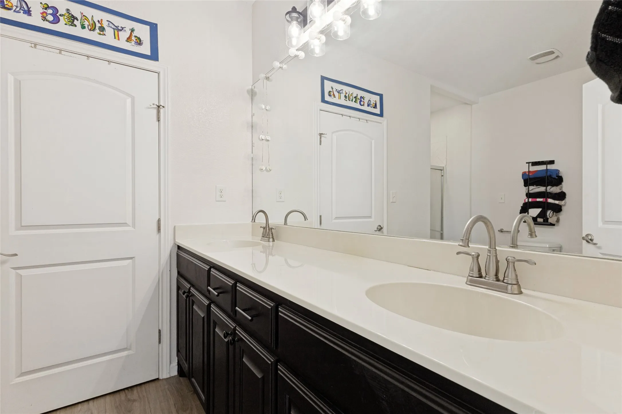 Dual vanity with an integrated sink and brushed nickel fixtures, dark wood-finish cabinetry, and wood-finish flooring