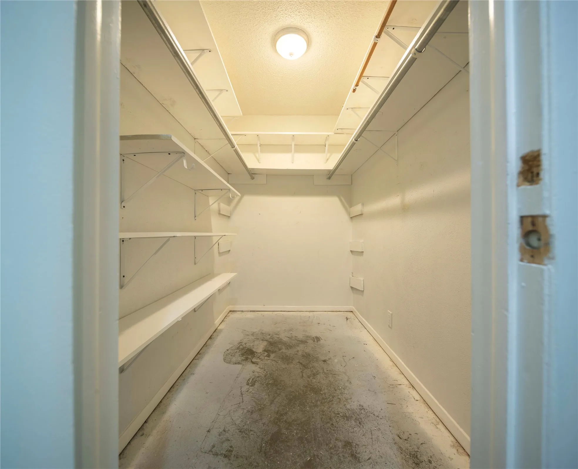 Built-in shelving and hanging rods in a walk-in closet with overhead lighting