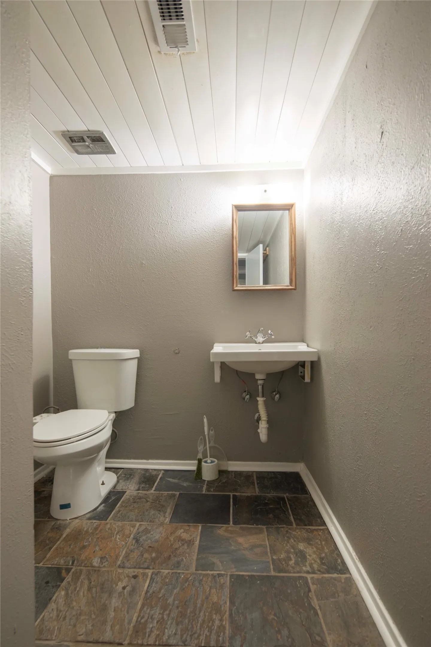 Plank panel ceiling, wall-mounted sink, framed mirror, and multi-tone tile flooring