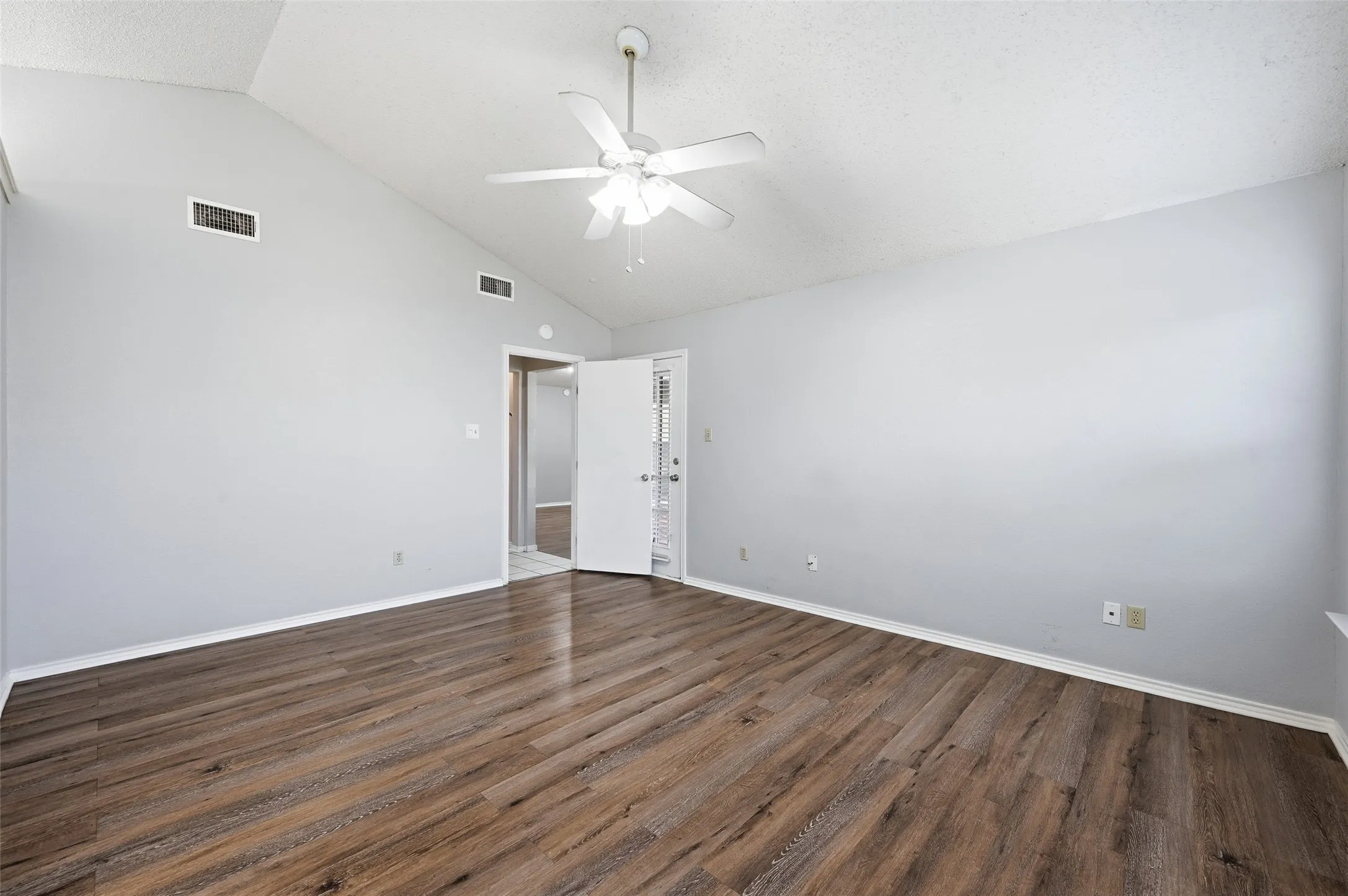 Vaulted ceiling with a white ceiling fan, wood-finish flooring, and light-toned walls