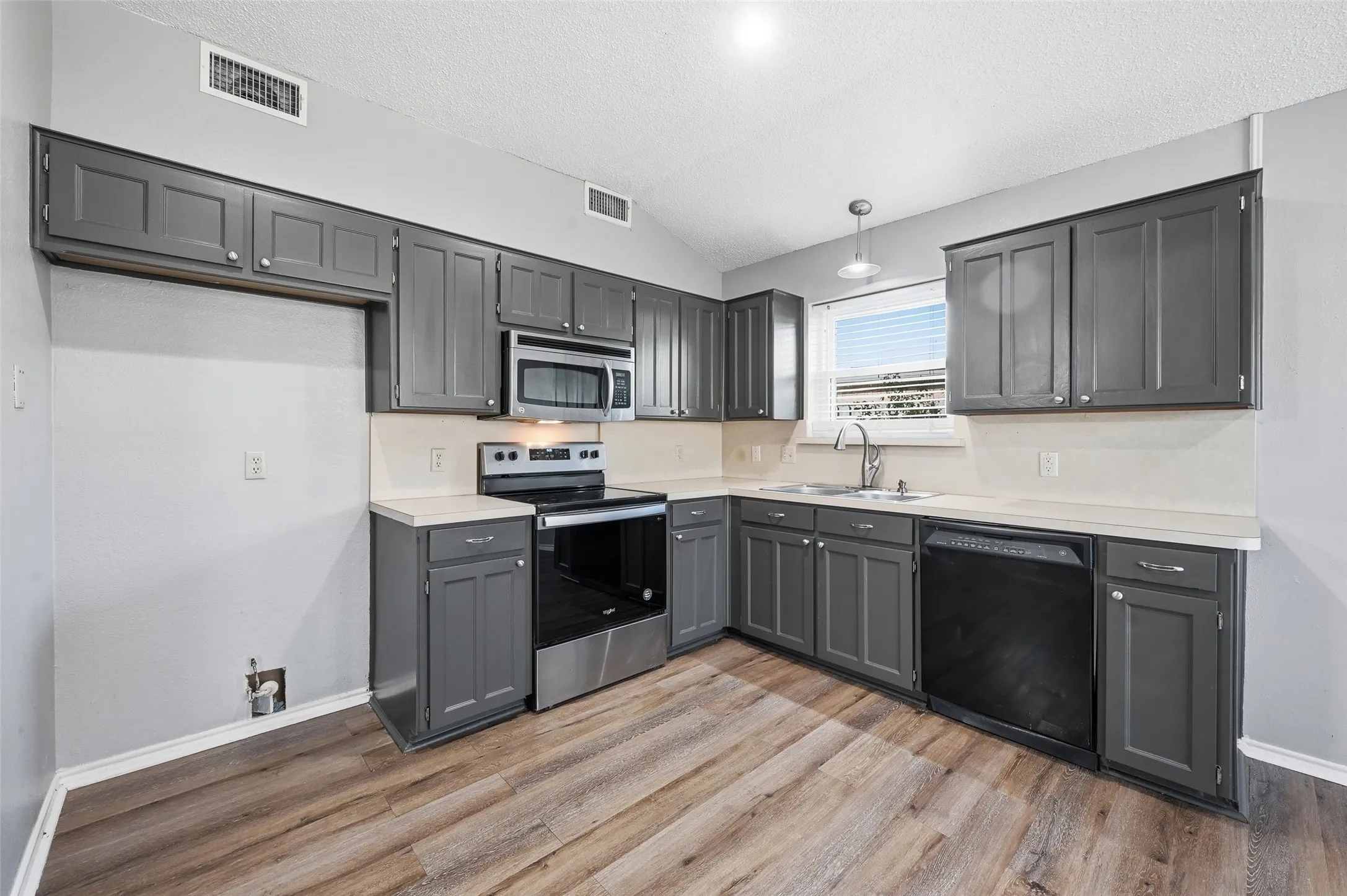 Kitchen featuring abundant gray cabinetry, light-toned countertops, wood-finish flooring, stainless steel microwave, and a stainless steel range