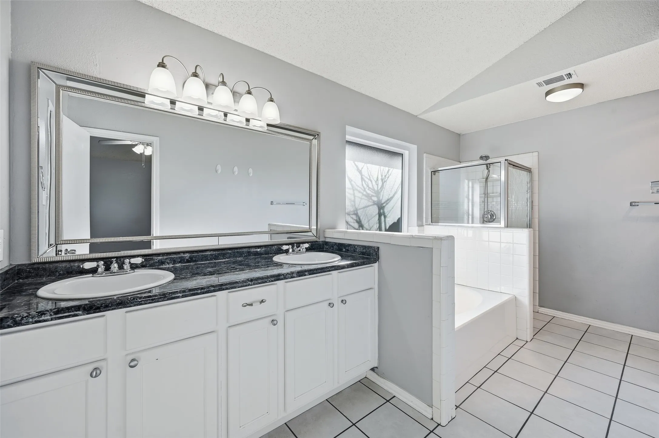 Dual vanity with undermount sinks, stone-finish countertop, white cabinetry, a framed mirror, and a built-in shower and tub combination