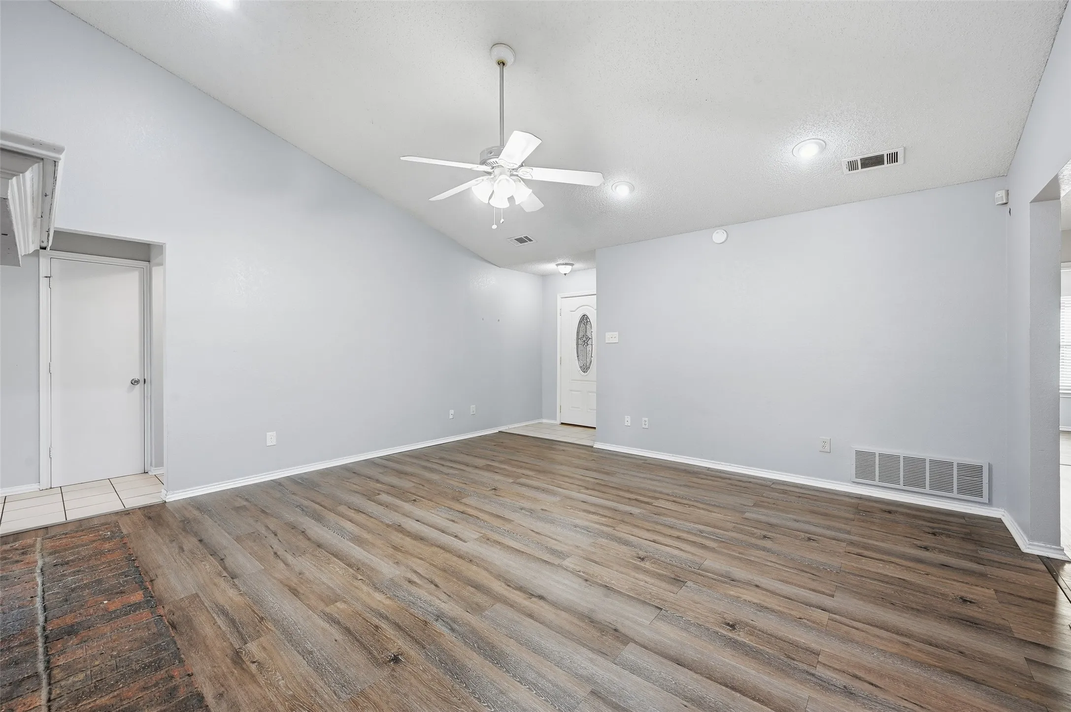 Vaulted ceiling, wood-finish flooring, ceiling fan, recessed lighting, and a front entry door with an oval glass insert